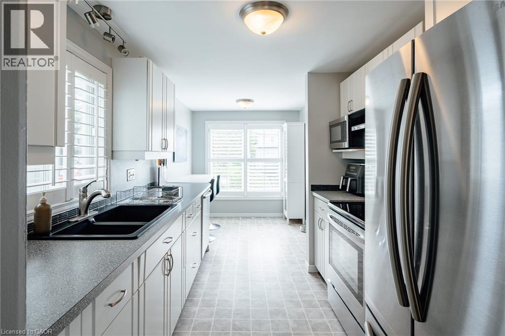 Galley kitchen featuring white cabinetry, stainless steel appliances, a double basin sink, and shuttered windows - 560 Penny Lane, Waterloo, ON