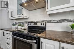 Kitchen featuring white cabinetry with dark hardware, dark countertops, and a subway tile backsplash with an accent band -
