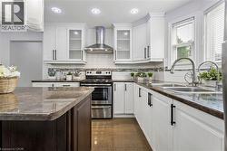 Kitchen featuring white cabinetry with dark hardware, a stainless steel range with overhead hood, and a tile backsplash -