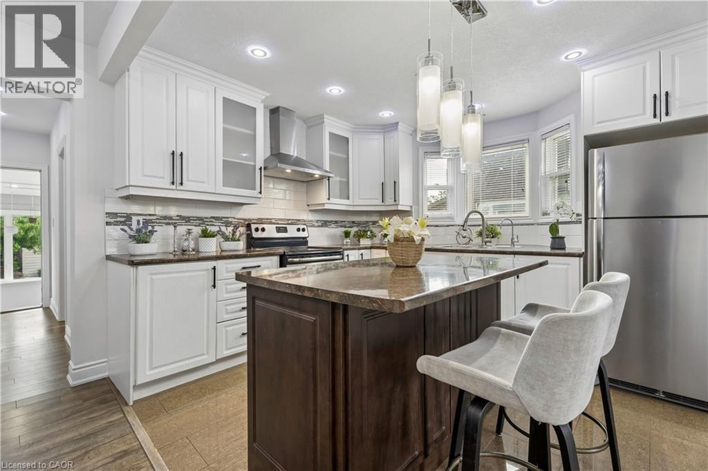 Bright kitchen featuring white cabinetry, a built-in stainless steel range hood, stone countertops, a tiled backsplash, and recessed lighting - 180 Campbell Avenue, Hamilton, ON - Indoor Photo Showing Kitchen With Upgraded Kitchen