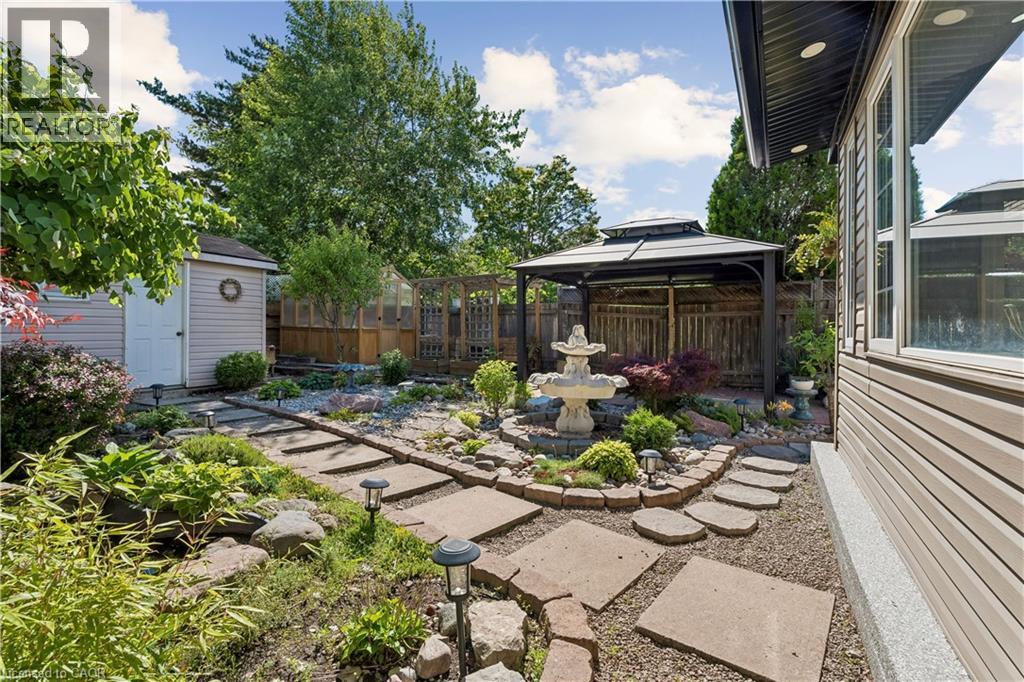 Landscaped backyard featuring a decorative stone fountain, a gazebo with a metal roof, and a garden shed - 180 Campbell Avenue, Hamilton, ON - Outdoor