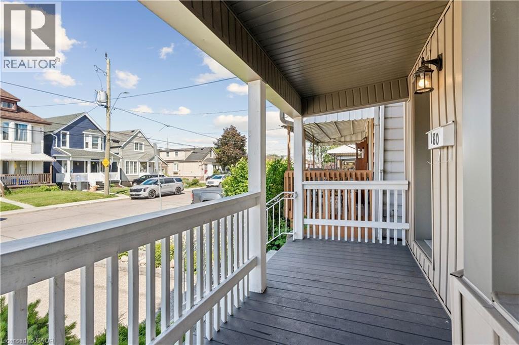 Covered front porch featuring white railing, dark wood-finish flooring, and a wall-mounted exterior light fixture - 180 Campbell Avenue, Hamilton, ON - Outdoor With Deck Patio Veranda With Exterior