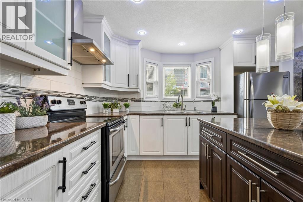 Contemporary kitchen featuring white cabinetry with dark hardware, dark countertops, stainless steel appliances, a tile backsplash, and wood-finish flooring - 180 Campbell Avenue, Hamilton, ON - Indoor Photo Showing Kitchen With Upgraded Kitchen