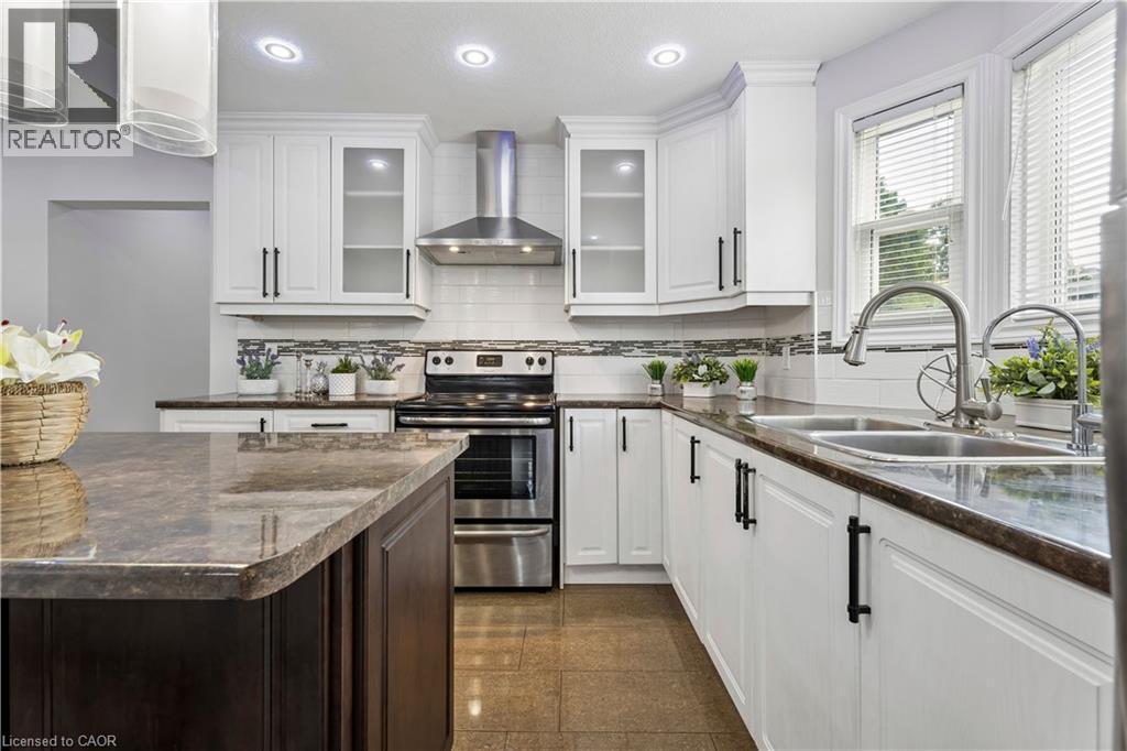 Kitchen featuring white cabinetry with dark hardware, a stainless steel range with overhead hood, and a tile backsplash - 180 Campbell Avenue, Hamilton, ON - Indoor Photo Showing Kitchen With Double Sink With Upgraded Kitchen