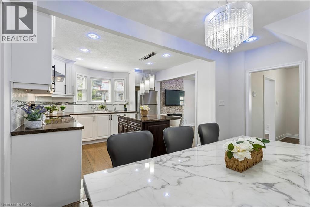 Spacious kitchen and dining area featuring a white marble-patterned dining table, a decorative chandelier, recessed lighting, and a kitchen with white cabinetry, dark countertops, and a tile backsplas - 180 Campbell Avenue, Hamilton, ON - Indoor Photo Showing Dining Room