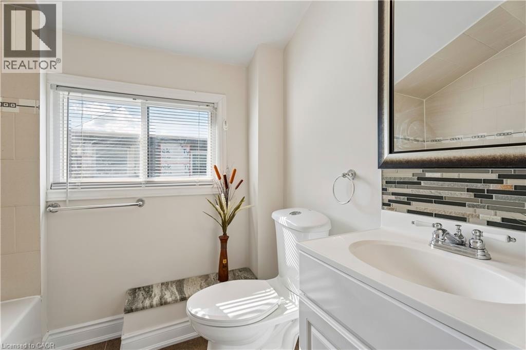 Bathroom featuring a window with blinds, a white vanity with an integrated sink, a chrome faucet, and a decorative tile backsplash - 180 Campbell Avenue, Hamilton, ON - Indoor Photo Showing Bathroom