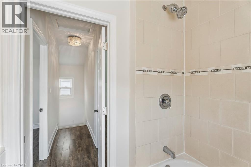 Bathroom shower with beige tile surround, decorative accent band, and chrome fixtures - 180 Campbell Avenue, Hamilton, ON - Indoor Photo Showing Bathroom