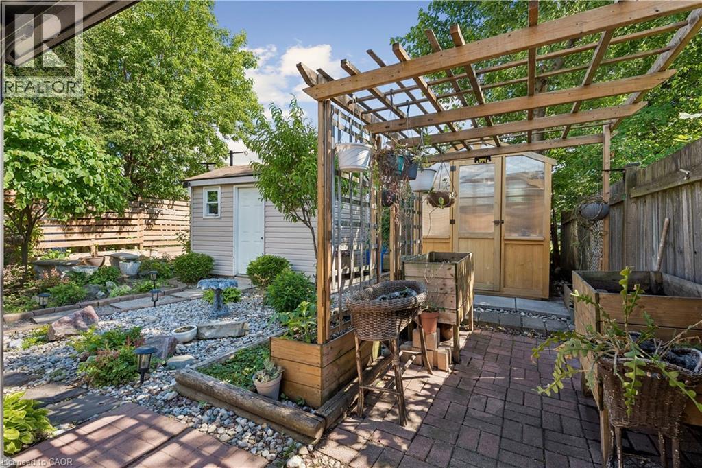 Expansive backyard featuring a brick paver patio, a wooden pergola, a dedicated greenhouse structure, a garden shed, and varied landscaping with mature trees and stone pathways - 180 Campbell Avenue, Hamilton, ON - Outdoor With Deck Patio Veranda