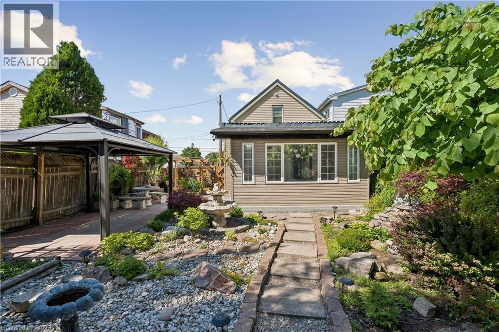 Inviting backyard featuring extensive landscaping, a stone pathway, and a central water feature - 180 Campbell Avenue, Hamilton, ON - Outdoor