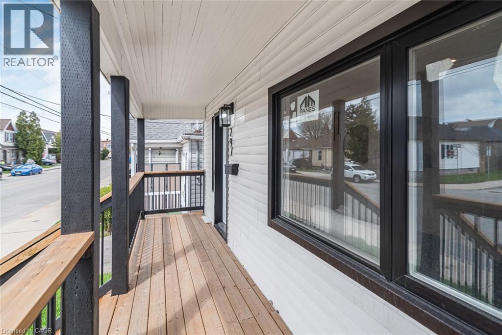 Covered porch with wood-finish flooring, dark-stained railings, and white siding - 297 Britannia Avenue, Hamilton, ON