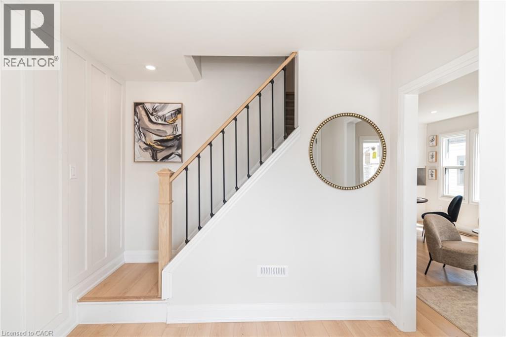 Light wood-finish flooring throughout, featuring a staircase with wood banister and black metal spindles - 297 Britannia Avenue, Hamilton, ON