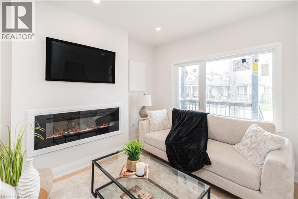 Contemporary living area featuring a wall-mounted linear electric fireplace beneath a mounted television - 297 Britannia Avenue, Hamilton, ON
