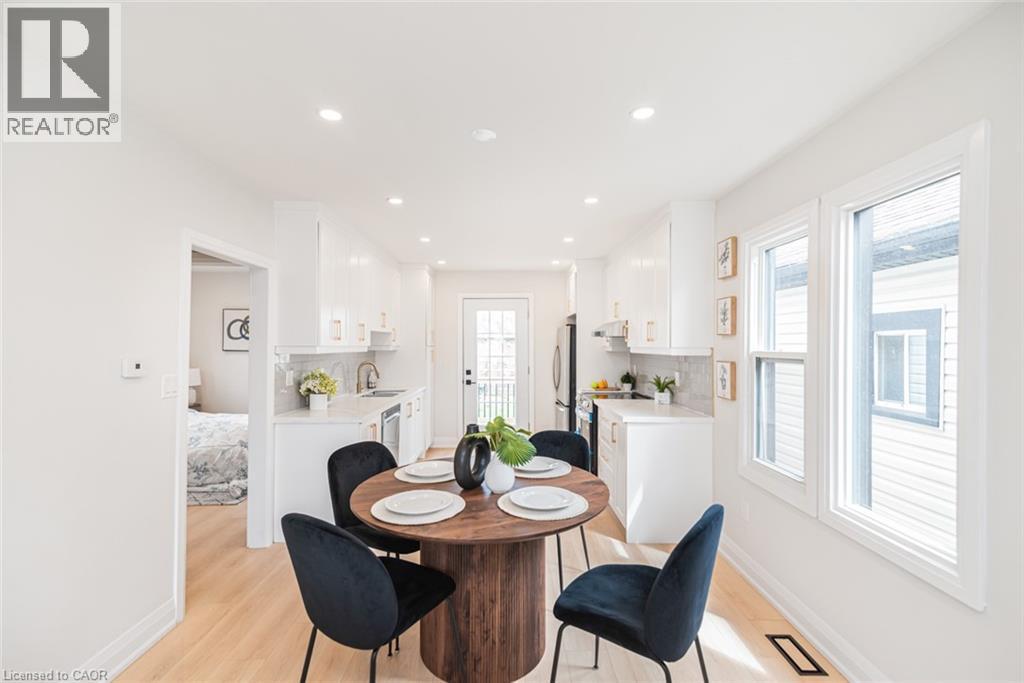Open-concept kitchen and dining area featuring light wood-finish flooring, white cabinetry, recessed lighting, and ample natural light from multiple windows - 297 Britannia Avenue, Hamilton, ON