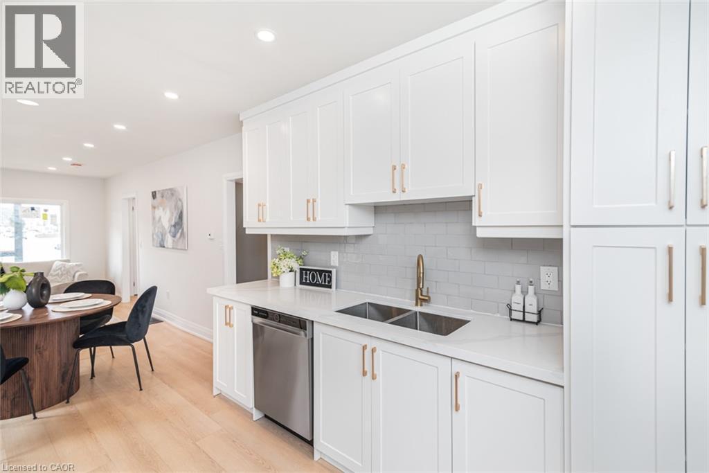 Kitchen featuring white cabinetry with gold-finish hardware, light grey subway tile backsplash, and light countertops - 297 Britannia Avenue, Hamilton, ON