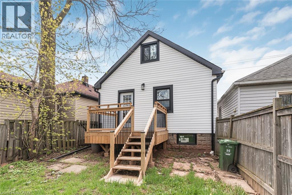 Rear exterior featuring white horizontal siding, black trim windows, and a dark shingled roofline - 297 Britannia Avenue, Hamilton, ON