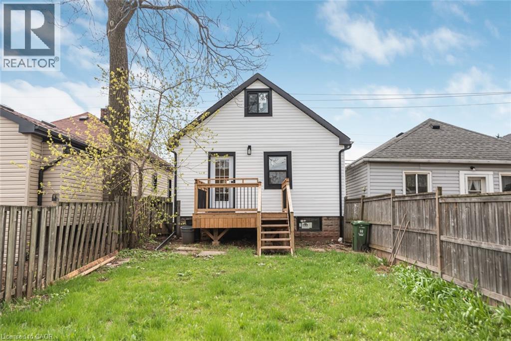 Rear exterior featuring white horizontal siding, a gabled roof with dark shingles, and black trim windows - 297 Britannia Avenue, Hamilton, ON