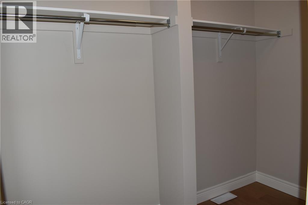 Spacious walk-in closet featuring dual clothing rods with metal brackets, white painted walls, and wood-finish flooring - 8 Dunlop Road, Hamilton, ON - Indoor Photo Showing Other Room