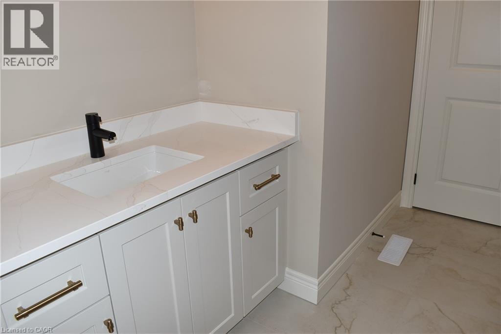 Elegant primary bathroom vanity featuring a white shaker-style cabinetry with brass hardware, quartz countertop, rectangular undermount sink, and matte black wall-mounted faucet - 8 Dunlop Road, Hamilton, ON - Indoor