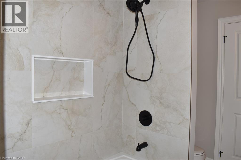 Shower enclosure featuring large format stone-finish wall tile, built-in recessed niche, and matte black shower fixtures with a handheld spray - 8 Dunlop Road, Hamilton, ON - Indoor Photo Showing Bathroom