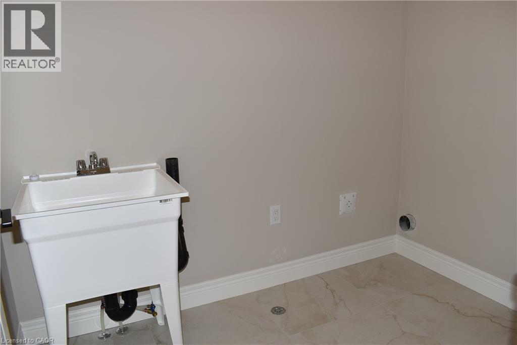 Utility room featuring a laundry sink with chrome faucet, light neutral wall paint, white baseboards, and tile flooring - 8 Dunlop Road, Hamilton, ON - Indoor