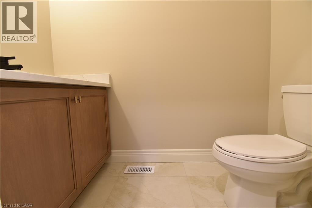 Clean, functional bathroom featuring a white porcelain toilet with soft-close seat, wood-finish vanity with dual handles, ceramic tile flooring, and neutral wall finishes - 8 Dunlop Road, Hamilton, ON - Indoor Photo Showing Bathroom
