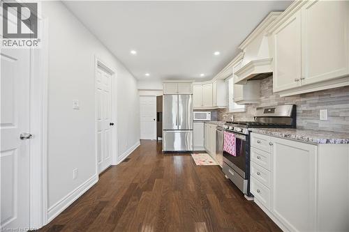 Contemporary kitchen featuring white cabinetry, stainless steel appliances, speckled countertops, a tiled backsplash, and wood-finish flooring - 71 Beland Avenue N, Hamilton, ON 