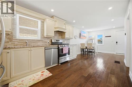 Open concept kitchen featuring cream-colored cabinetry, stone-finish countertops, stainless steel appliances, and wood-finish flooring - 71 Beland Avenue N, Hamilton, ON 
