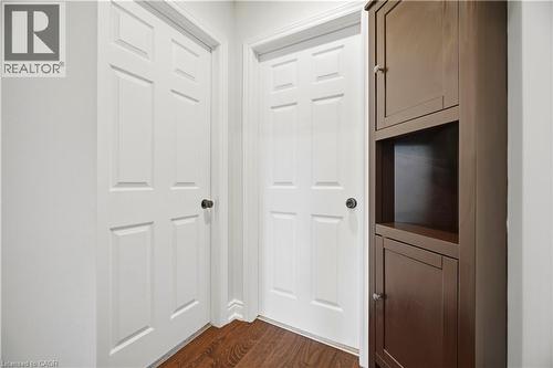 Hallway featuring wood-finish flooring, two white paneled doors with dark hardware, and a built-in dark wood storage cabinet with open shelving - 71 Beland Avenue N, Hamilton, ON 