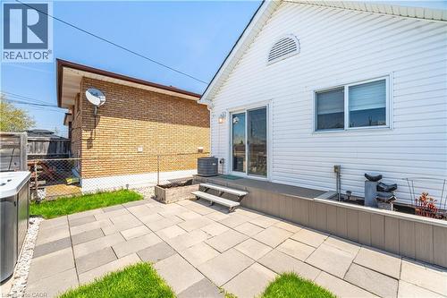 Expansive backyard featuring a paver patio with integrated green spaces, a raised composite deck, and white vinyl siding - 71 Beland Avenue N, Hamilton, ON 