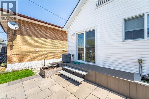 Rear exterior featuring white horizontal siding, a sliding glass patio door, and an exterior window with blinds - 71 Beland Avenue N, Hamilton, ON 