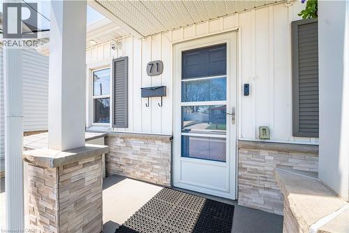 Front entry featuring a white screen door, vertical white siding, and a stone veneer foundation - 71 Beland Avenue N, Hamilton, ON 
