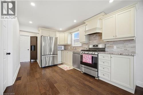 Kitchen featuring cream cabinetry, stainless steel appliances, wood-finish flooring, a mosaic tile backsplash, and recessed lighting - 71 Beland Avenue N, Hamilton, ON 