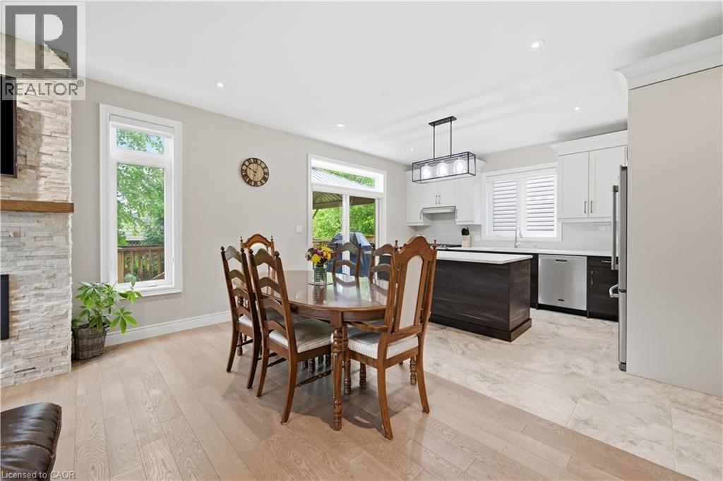 Open-concept living space featuring wood-finish flooring, a stacked stone fireplace with a wood mantel, and large windows - 1 Lindsay Way, Grimsby, ON - Indoor Photo Showing Dining Room With Fireplace