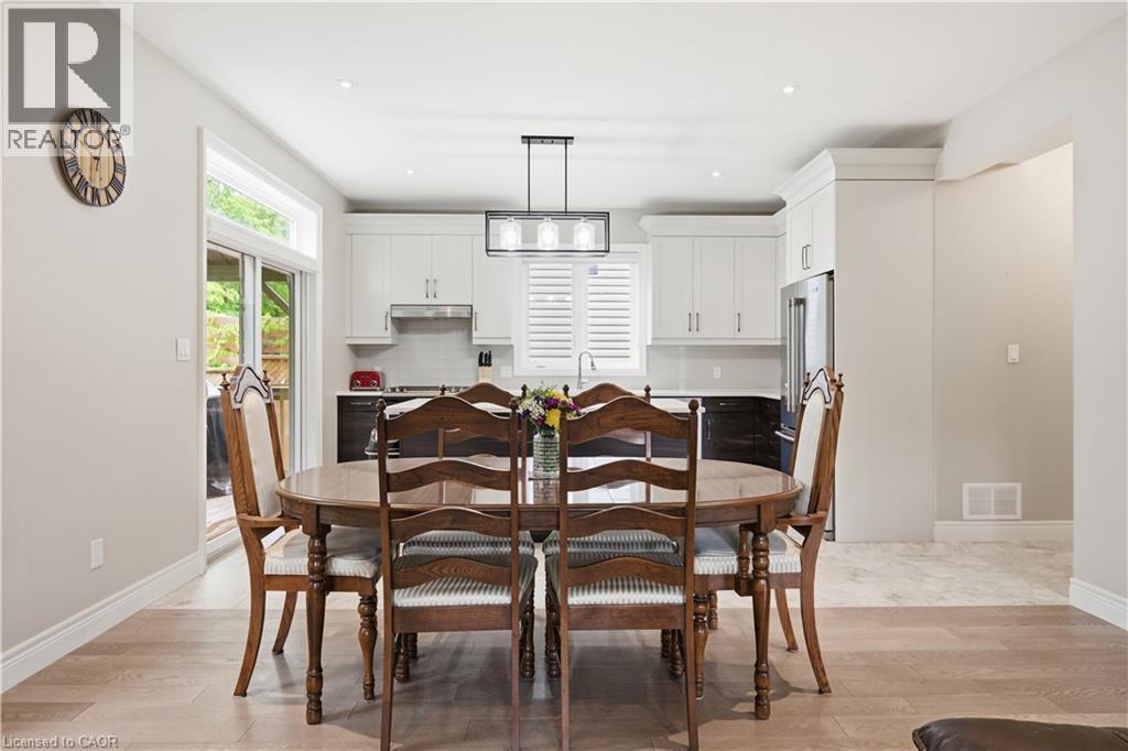 Open-concept dining area featuring wood-finish flooring, a modern linear chandelier, and a sliding glass door - 1 Lindsay Way, Grimsby, ON - Indoor Photo Showing Dining Room