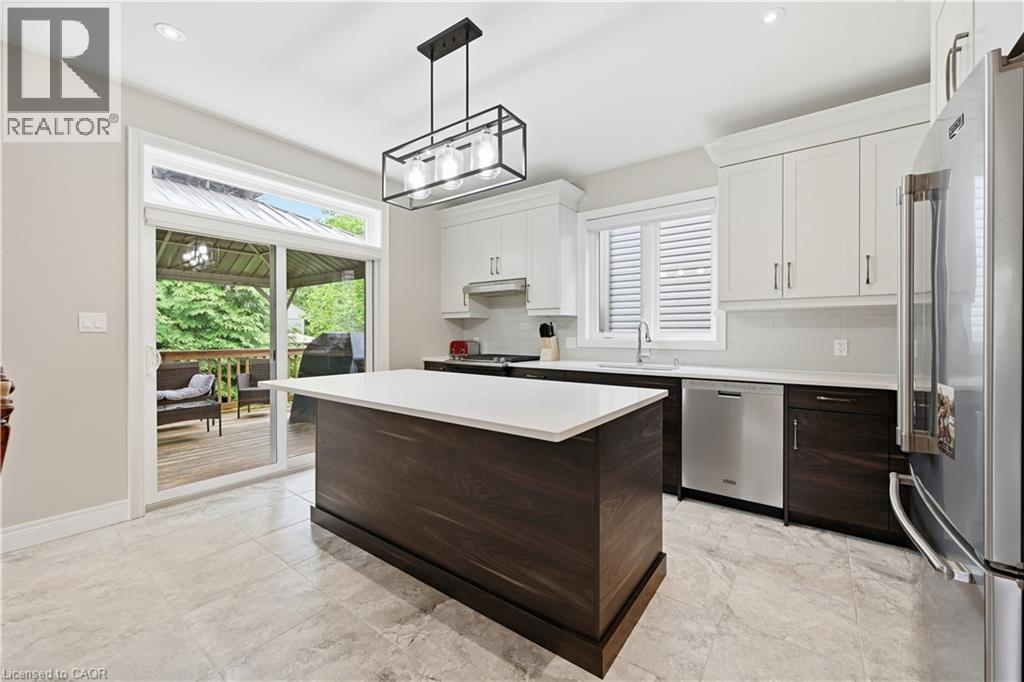 Kitchen featuring a large central island with a solid surface countertop, light-toned tiled flooring, white upper cabinetry, dark wood-finish lower cabinetry, and stainless steel appliances - 1 Lindsay Way, Grimsby, ON - Indoor Photo Showing Kitchen With Upgraded Kitchen