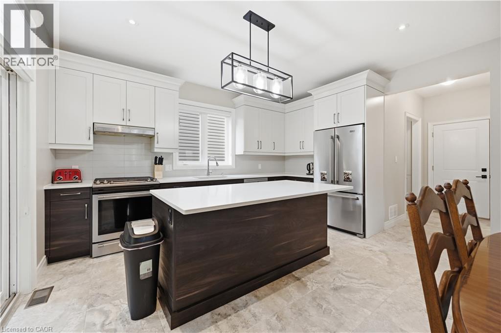 Modern kitchen featuring white upper cabinetry, dark wood-finish lower cabinetry, and a central island with a white countertop - 1 Lindsay Way, Grimsby, ON - Indoor Photo Showing Kitchen With Upgraded Kitchen