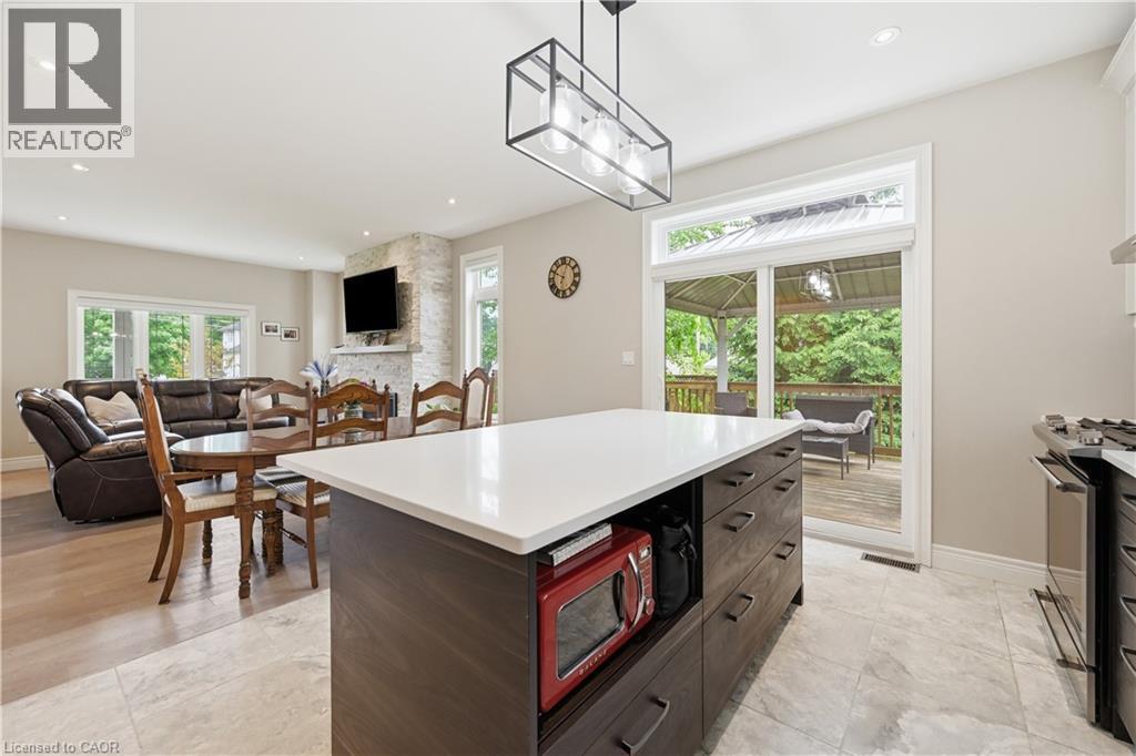 Open-concept interior featuring a central kitchen island with a light-toned countertop, a built-in cooktop, and a sliding glass door leading to an exterior deck - 1 Lindsay Way, Grimsby, ON - Indoor