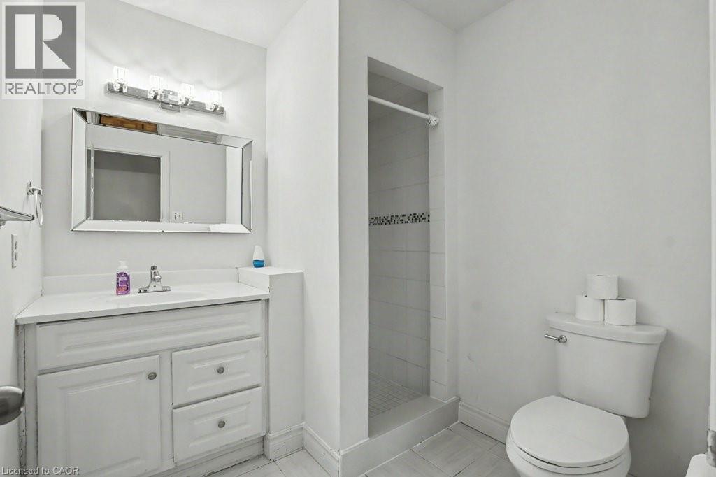 Bathroom featuring a single vanity with storage, a rectangular mirror, and a walk-in shower with decorative tile accent - 396 Pinemeadow Avenue, Mississauga, ON