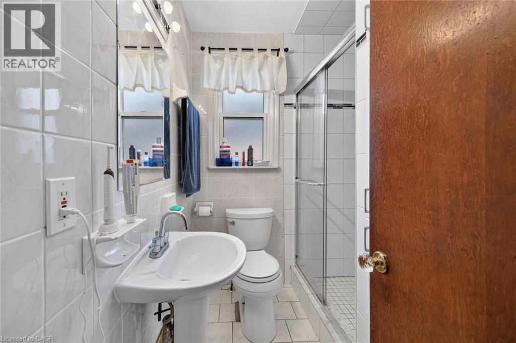 Bathroom featuring a pedestal sink, chrome faucet, and a wall-mounted mirror with overhead lighting - 83 Aberfoyle Avenue, Hamilton, ON