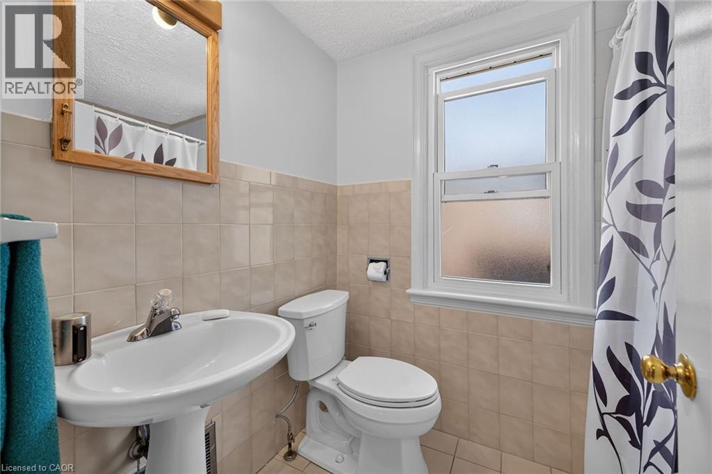 Pedestal sink with chrome faucet, light-colored square wall tiles, and wood-framed mirror - 83 Aberfoyle Avenue, Hamilton, ON