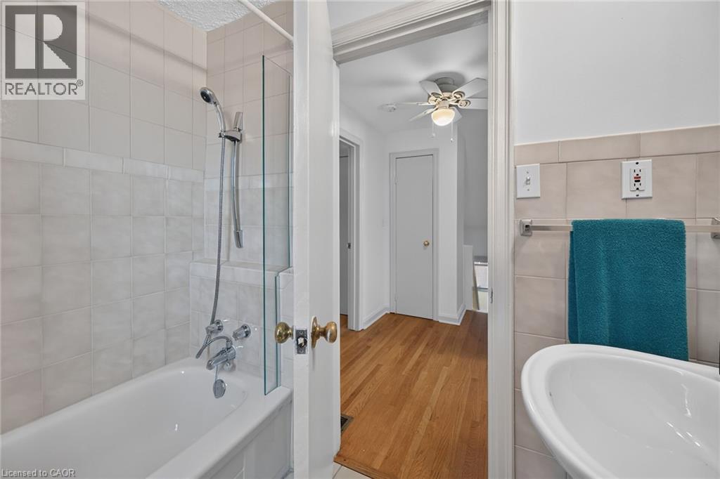 Bathroom featuring a white bathtub, ceramic tile surround, and a glass shower partition - 83 Aberfoyle Avenue, Hamilton, ON