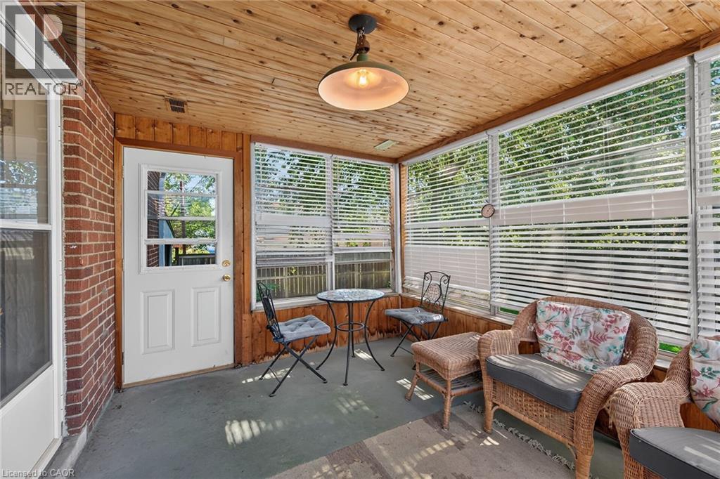 Enclosed porch featuring a wood-panel ceiling, brick wall, wood-paneled accent wall, screened windows with blinds, and a white exterior door with window panes - 83 Aberfoyle Avenue, Hamilton, ON