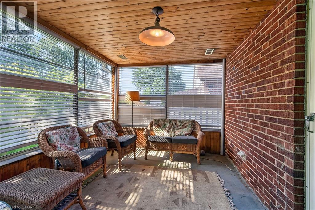 Screened-in porch featuring a natural wood plank ceiling, exposed brick wall, multiple window panels with blinds, and a central ceiling light fixture - 83 Aberfoyle Avenue, Hamilton, ON