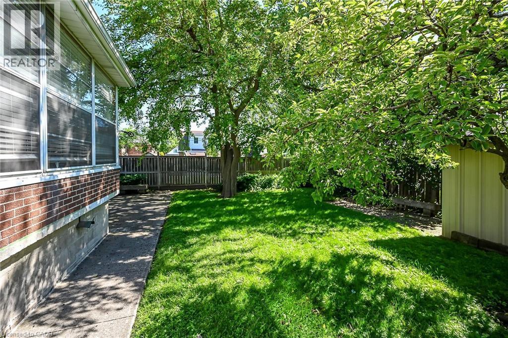 Expansive green lawn with mature trees and a concrete pathway alongside the brick and concrete foundation - 83 Aberfoyle Avenue, Hamilton, ON