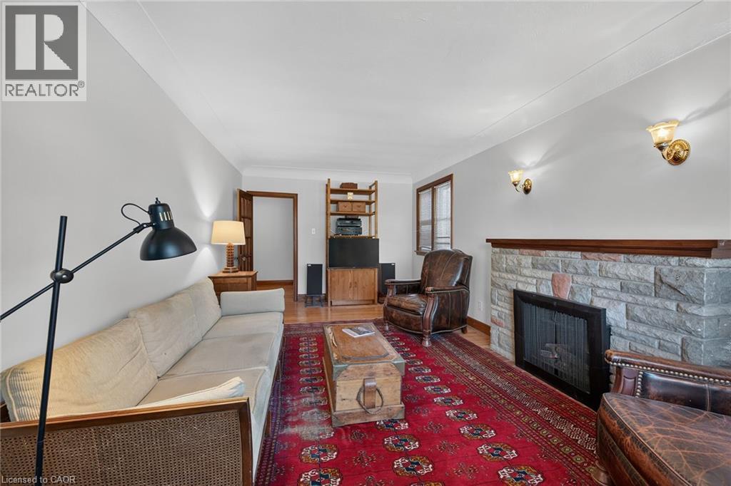 Living space featuring wood-finish flooring, a stone fireplace with a wood mantel, and brass wall sconces - 83 Aberfoyle Avenue, Hamilton, ON