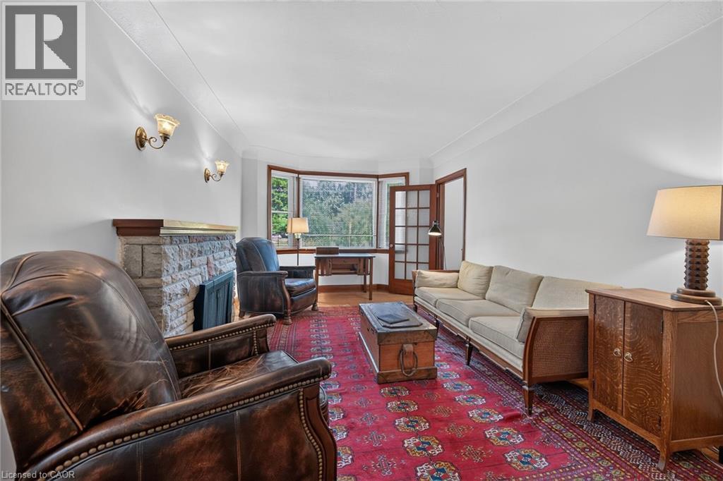 Spacious living area featuring a stone-clad fireplace with wood mantel, wall sconces, wood-frame bay windows, and wood-finish flooring - 83 Aberfoyle Avenue, Hamilton, ON