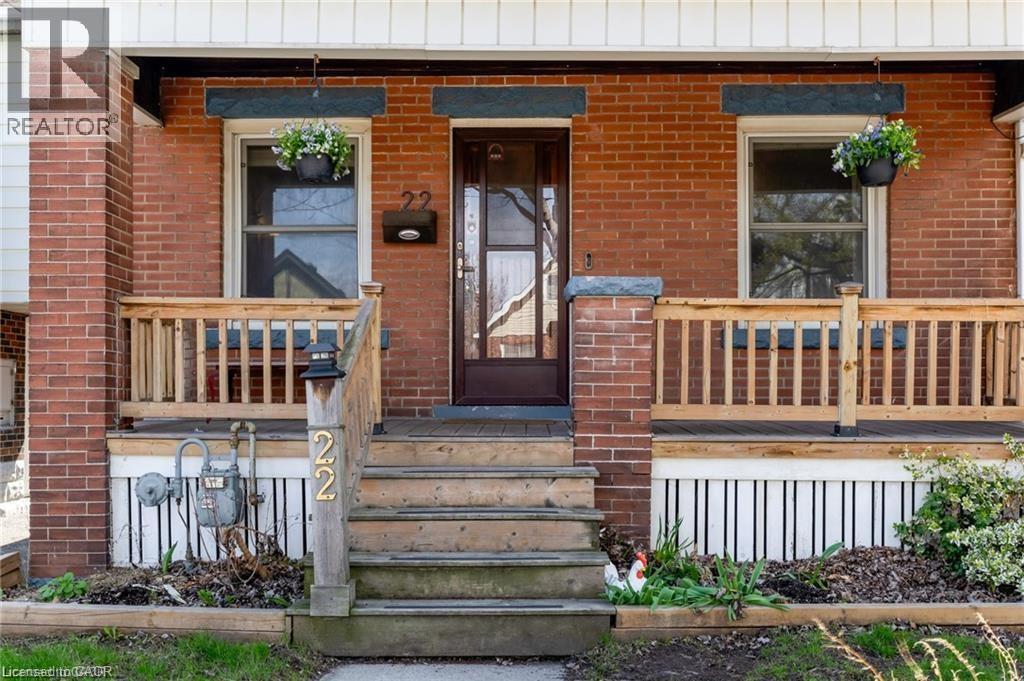 Brick exterior featuring a covered porch with natural wood railings, wood steps, and a dark-framed entry door - 22 Cope Street, Hamilton, ON