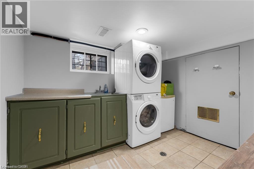 Dedicated laundry area featuring a stacked washer and dryer, a utility sink, and a countertop with storage cabinetry below - 22 Cope Street, Hamilton, ON