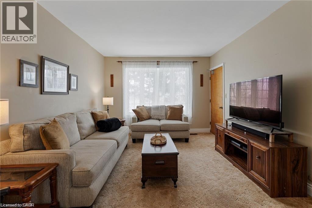 Carpeted living area featuring a large window, a wood-finish media console, and neutral wall tones - 2 Mill Street E, York, ON