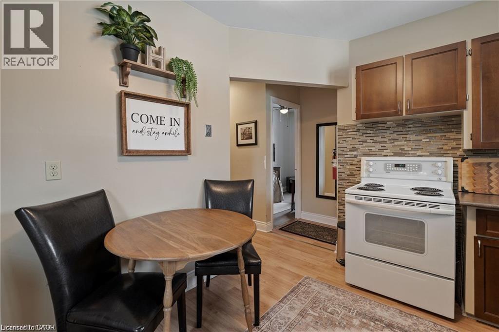Compact kitchen featuring a white electric range, mosaic tile backsplash, wood-finish flooring, and brown cabinetry - 2 Mill Street E, York, ON